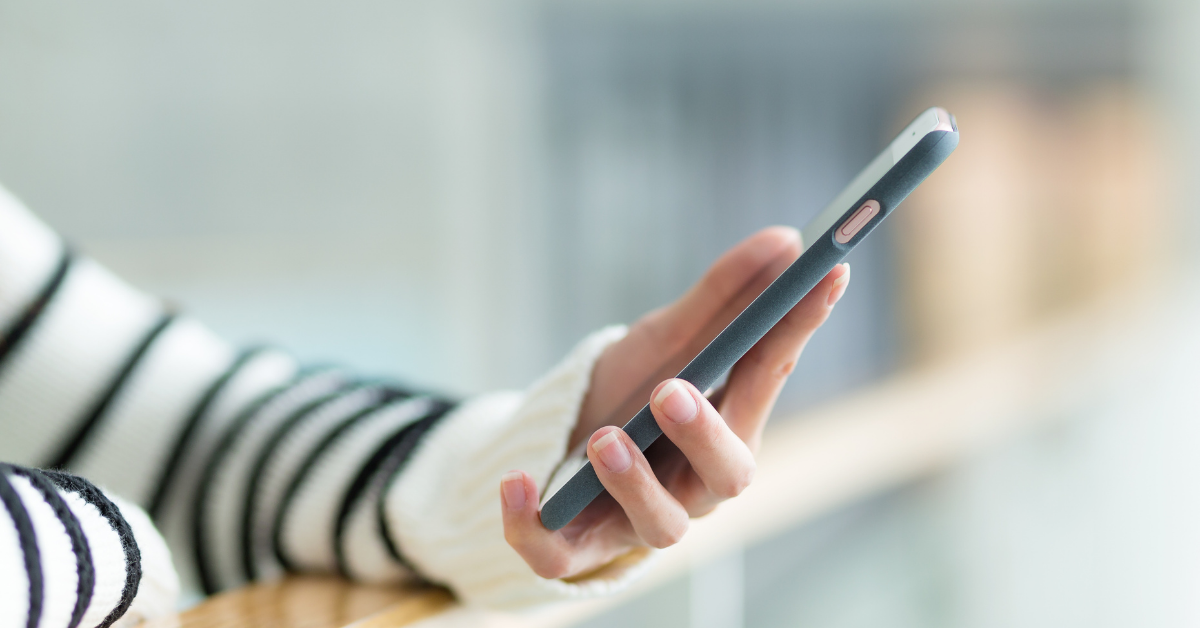 En hånd i stripete genser holder en smarttelefon