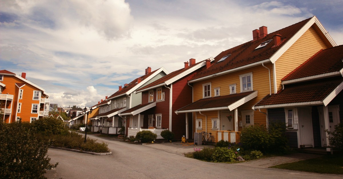 Rekkehus i gult, rødt og grått langs en boliggate, med en oransje boligblokk til venstre