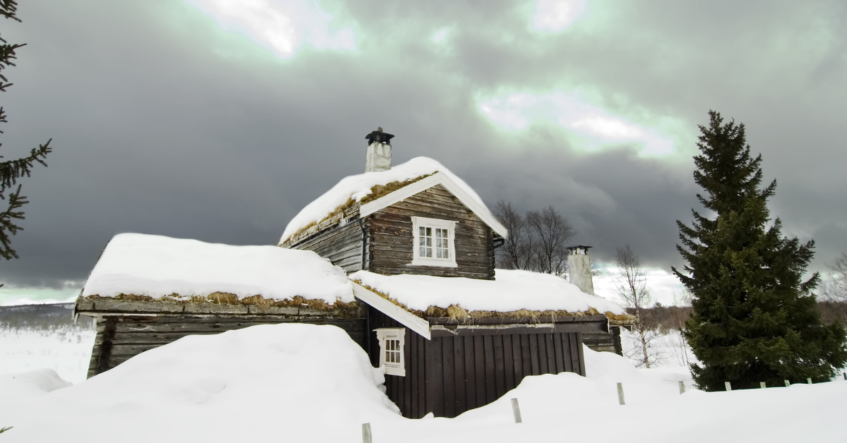 Gammel tømmerhytte med snø på taket midt på vinteren